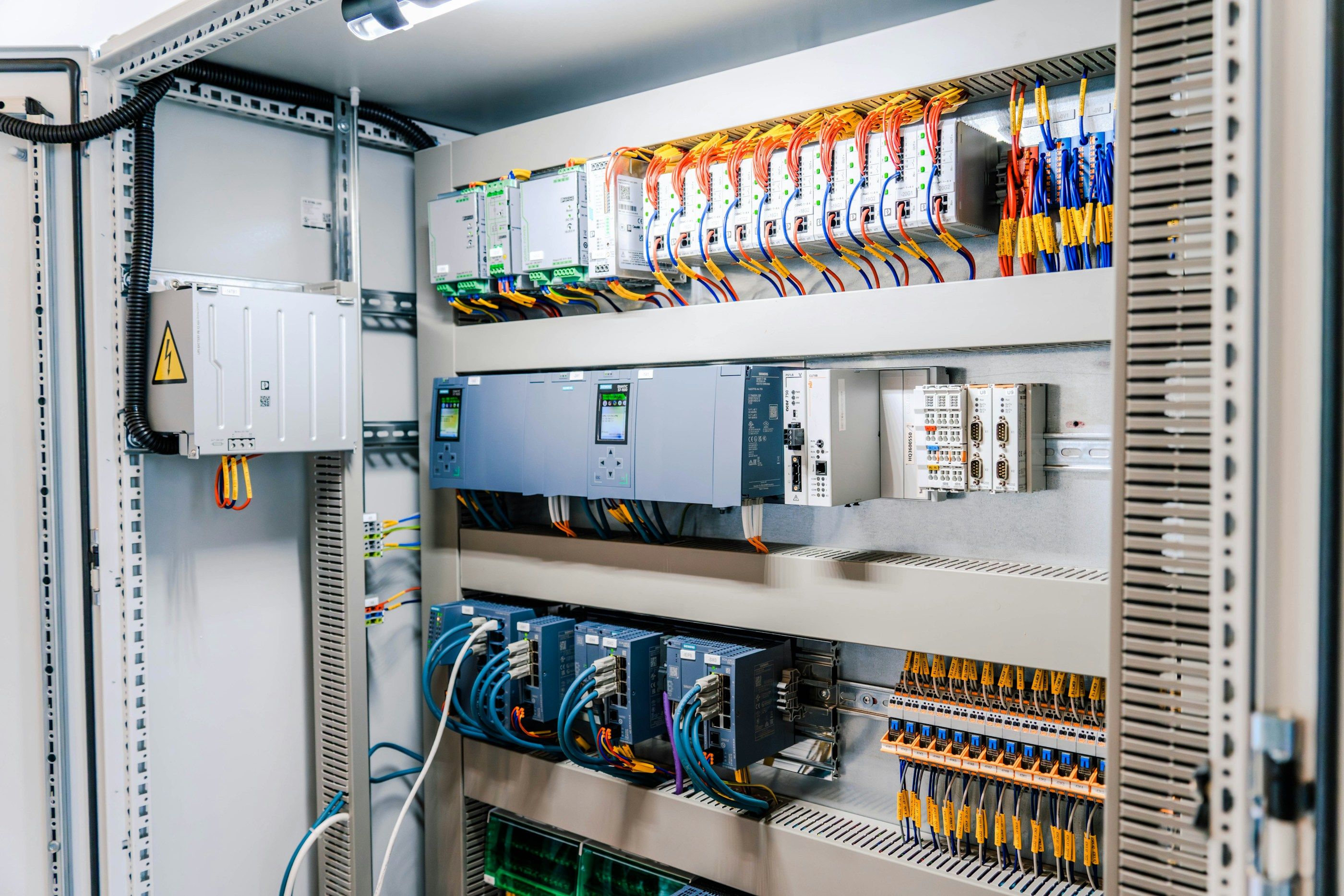 Geöffneter Schaltschrank mit Steuerungsmodulen, Netzwerk-Switches und farbig verdrahteten Klemmenreihen